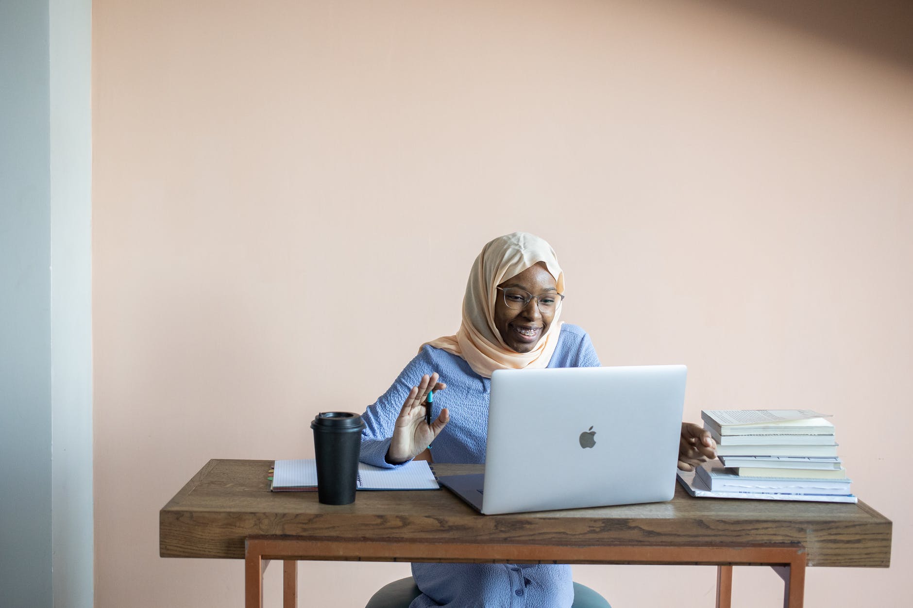 smiling muslim woman waving hand during online video call