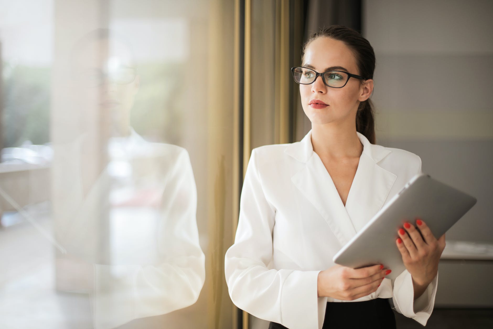 photo of woman in white top and glasses holding a tablet while looking outside a window thinking about Why It’s Ok To Quit And Move On From a Job