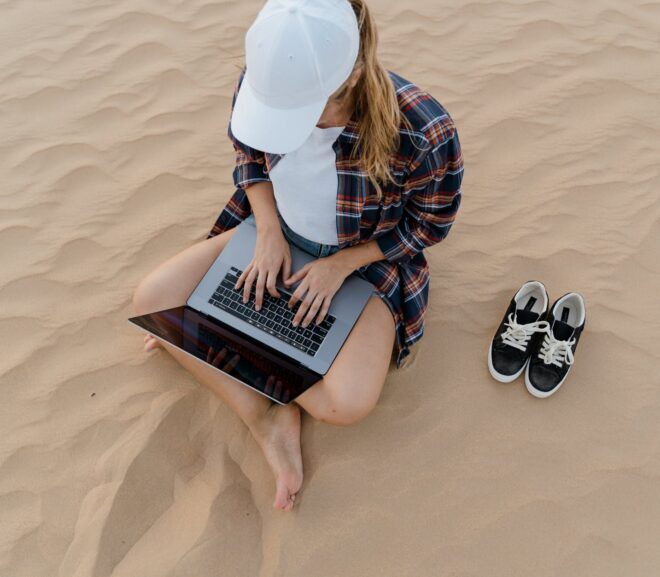 a woman typing on her laptop while sitting on sand