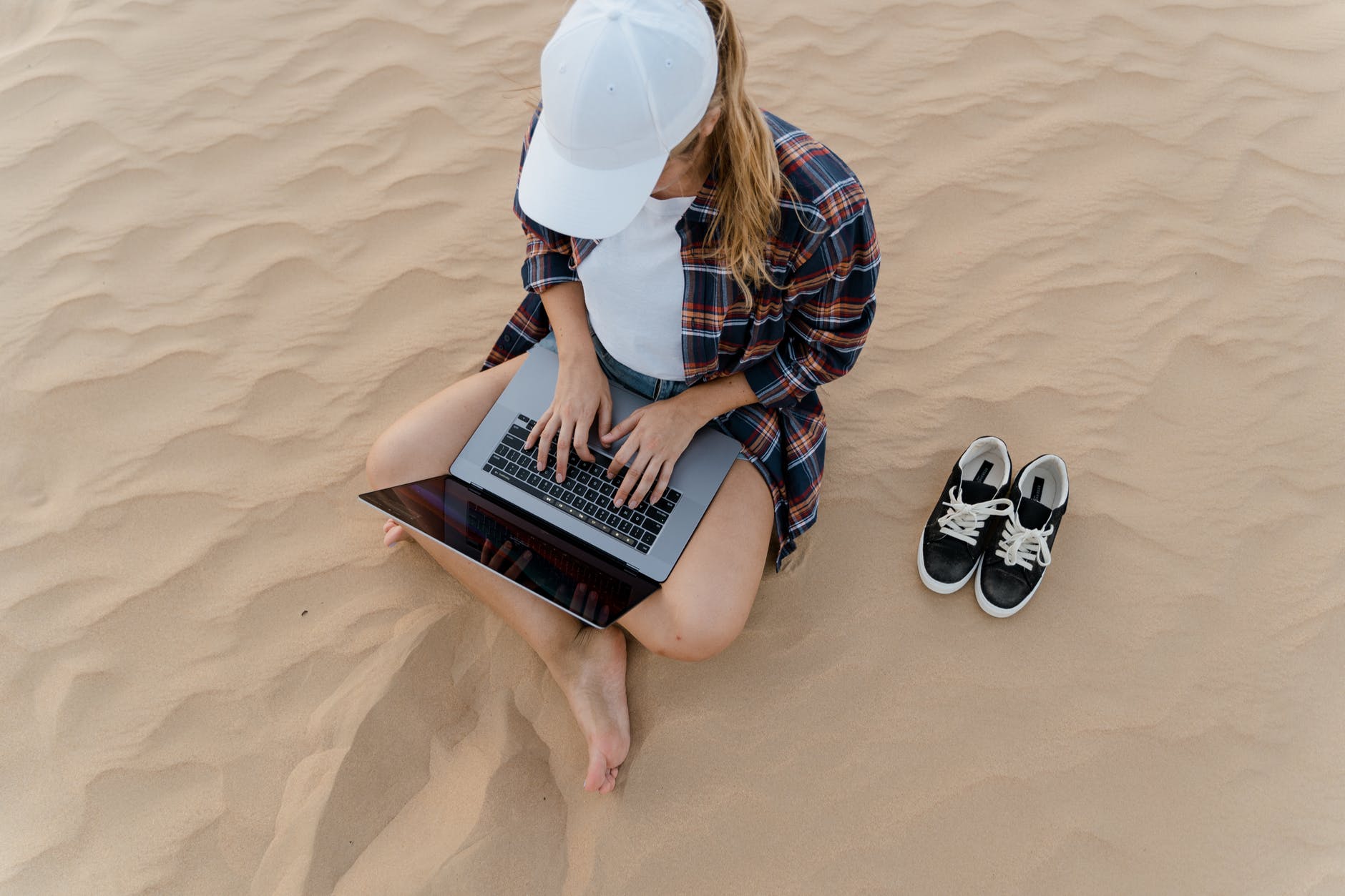 a woman typing on her laptop while sitting on sand, The Truth About Employee Benefits